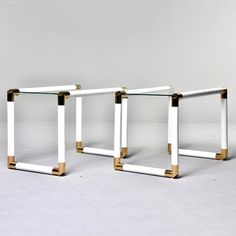 a pair of white and gold side tables with glass tops, each one has a square base