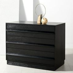 a black dresser with three drawers and a small vase on it's top shelf