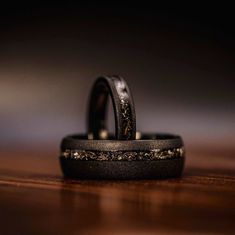 two wedding rings sitting on top of a wooden table next to each other with gold flecks