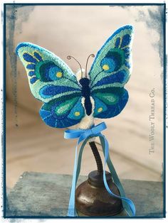 a blue and green butterfly sitting on top of a bell with a ribbon around it's neck