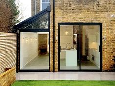 a brick building with glass doors and an open kitchen area in the back ground, next to a green lawn