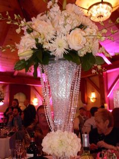 a tall vase filled with white flowers on top of a table next to other tables