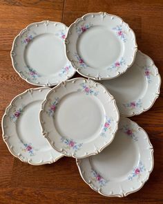 five white plates with pink and blue flowers are stacked on a wooden table, one is empty