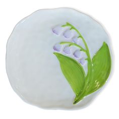 a white plate with green leaves and flowers painted on the side, in front of a white background