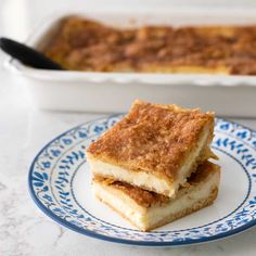 two pieces of cake on a blue and white plate next to a pan of food