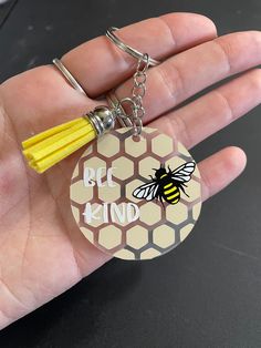 a hand holding a keychain with a bee kind on it