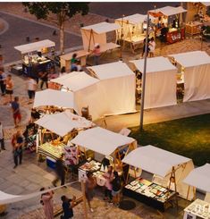 an aerial view of people walking around tents and tables in the middle of a park