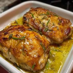 two pieces of chicken sitting on top of a white plate covered in oil and herbs