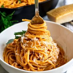 a fork full of spaghetti with sauce and parmesan cheese on top, in a white bowl