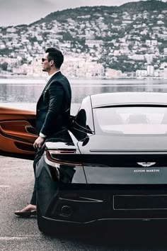 a man in a suit standing next to a black sports car and two canoes