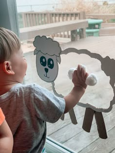 a young boy holding a paper sheep in front of a window with a sticker on it