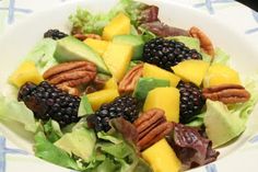 a white bowl filled with salad topped with fruit and nuts