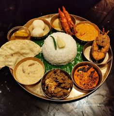 an assortment of different foods on a metal platter with rice and sauces in bowls