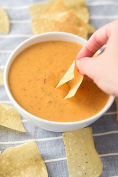 a person dipping tortilla chips into a bowl of salsa with tortilla chips on the side