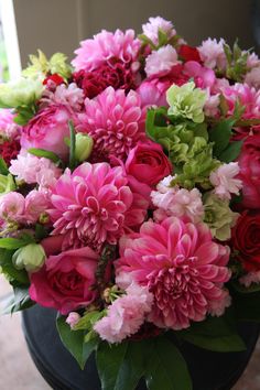 a bouquet of pink and red flowers in a black vase with green leaves on the side