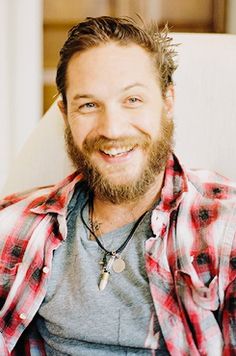 a man with a beard sitting in a chair smiling at the camera and wearing a plaid shirt