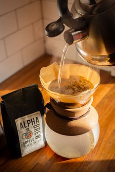 coffee being poured into a cup on top of a wooden table next to a bag of coffee