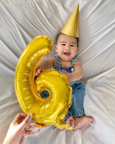 a baby wearing a party hat and holding a golden number balloon