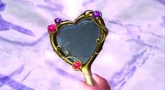 a heart shaped mirror being held up by someone's hand with jewels on it