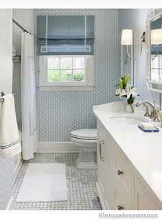 a white toilet sitting next to a bathroom sink under a window in a blue and white bathroom