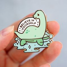 a person holding a pin with a rubber duck on it that says believe in yourself