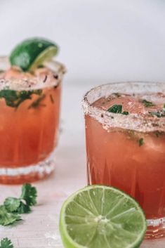 two cocktails with lime and mint garnish sit next to each other