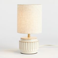 a white table lamp with a beige shade on the base and a cord attached to it