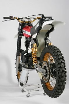 a white and black dirt bike parked on top of a metal stand in front of a white wall