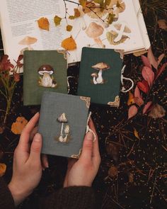 two hands holding small book covers with mushrooms on them