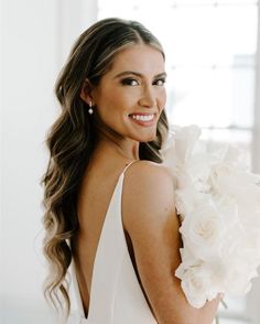 a beautiful woman in a white dress with flowers on her shoulder smiling at the camera