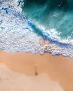 an aerial view of the beach and ocean with a lone person standing in the sand