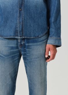 a man in blue jeans is holding his cell phone and looking at the camera while standing