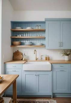 a kitchen with blue cabinets and wooden counter tops is pictured in this image, there are dishes on the shelves above the sink