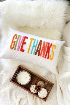 a pillow that says give thanks next to a tray with donuts and a candle