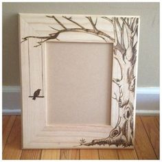 a wooden frame with a tree and bird painted on the inside, sitting on top of a hard wood floor