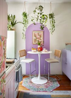 a small kitchen with purple walls and white table surrounded by chairs, potted plants on the wall