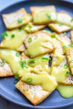 a blue plate topped with crackers covered in cheese and green sauce on top of it