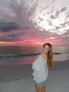 a woman standing on top of a sandy beach next to the ocean at sunset or dawn