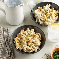 two bowls filled with pasta and vegetables on top of a table next to glasses of water