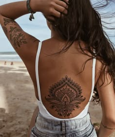 a woman with tattoos on her back standing at the beach