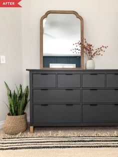 a black dresser with a mirror and potted plant on top in front of it