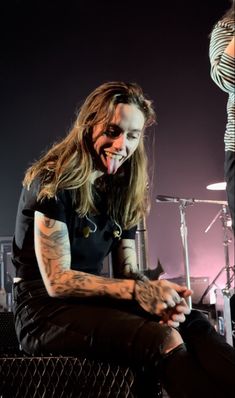 a man with long hair sitting on top of a bench next to a drum set