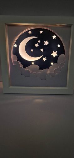 a night sky with stars and the moon lit up in a shadow box on top of a table