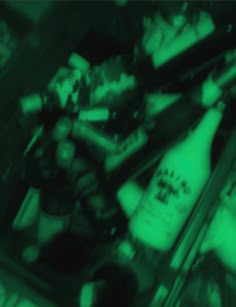 blurry photograph of bottles and cans in a store display case, with green lighting