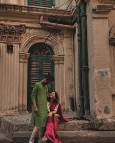 a man standing next to a woman in front of an old building with green doors