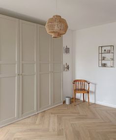 an empty room with white walls and wooden flooring has a wicker basket hanging from the ceiling