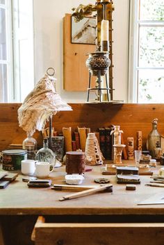 a wooden table topped with lots of clutter next to a tall window filled with windows