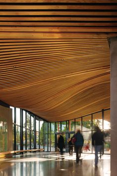 people are walking around in the lobby of an office building with large windows and wood slats on the ceiling