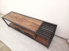 a wooden table with metal slats and drawers on the bottom, next to a white wall