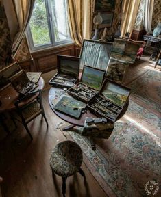 there are many paintings on the table in this room with two chairs and one chair